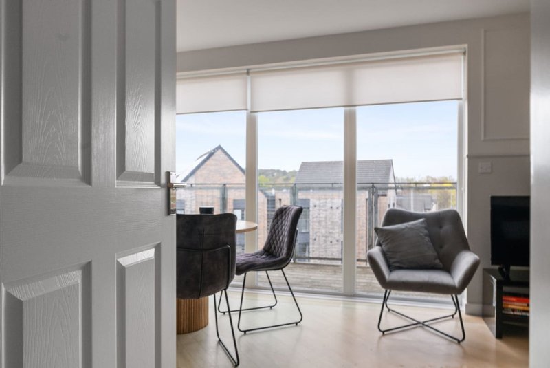 Modern living area with black chairs, armchair, and large windows overlooking residential neighborhood