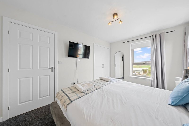 Bright bedroom with double bed, wall-mounted TV, window with countryside view, and white wardrobe