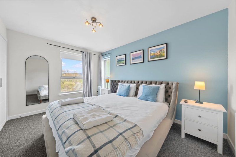 Modern bedroom with double bed, blue feature wall, white furniture and countryside view