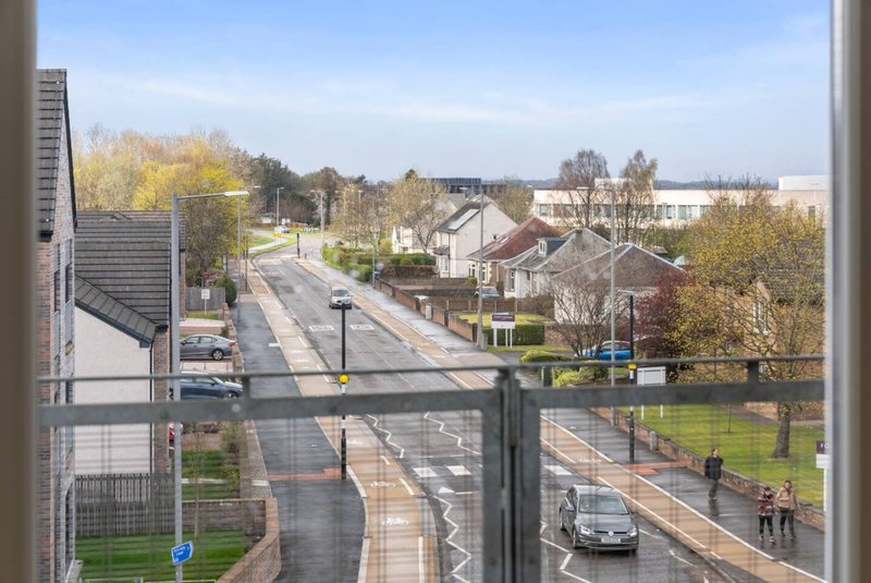 Street view from apartment window showing residential neighborhood with trees, parked cars and pedestrians