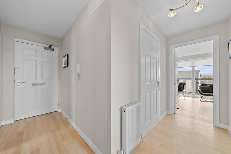 Bright hallway with light wood flooring, white doors and walls, leading to open-plan living area