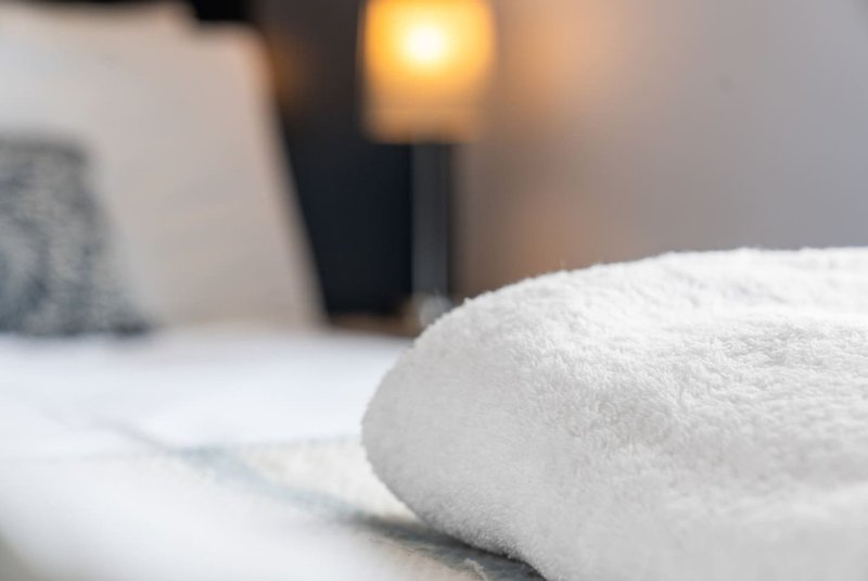 Close-up of white fluffy towel on bed with warm lamp and cushion in background
