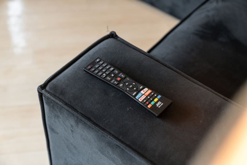 Remote control on dark upholstered armchair, wooden floor visible behind