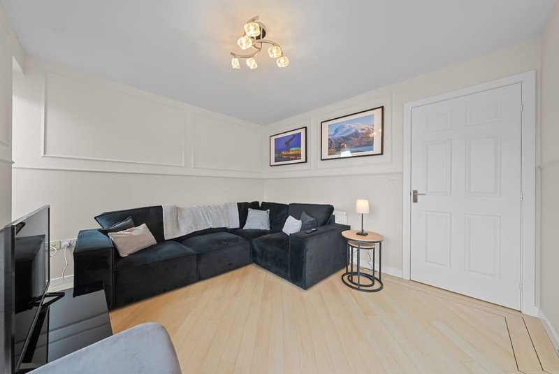Bright living room with black corner sofa, light wood flooring, white walls and ceiling light fixture