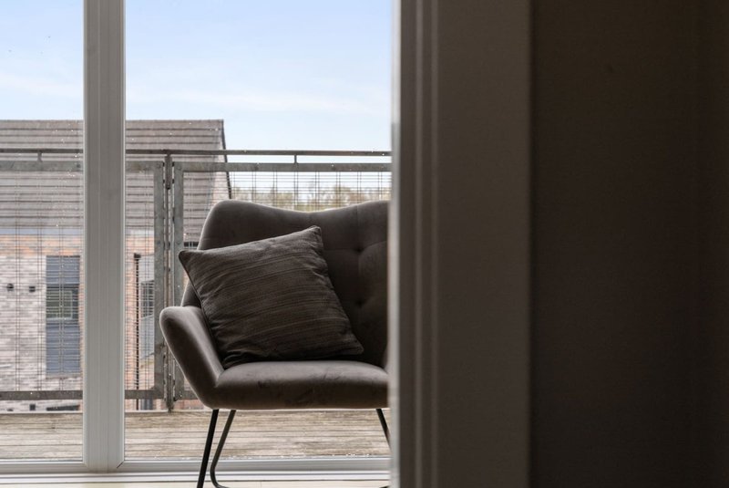 Modern armchair with cushion by large window overlooking urban street
