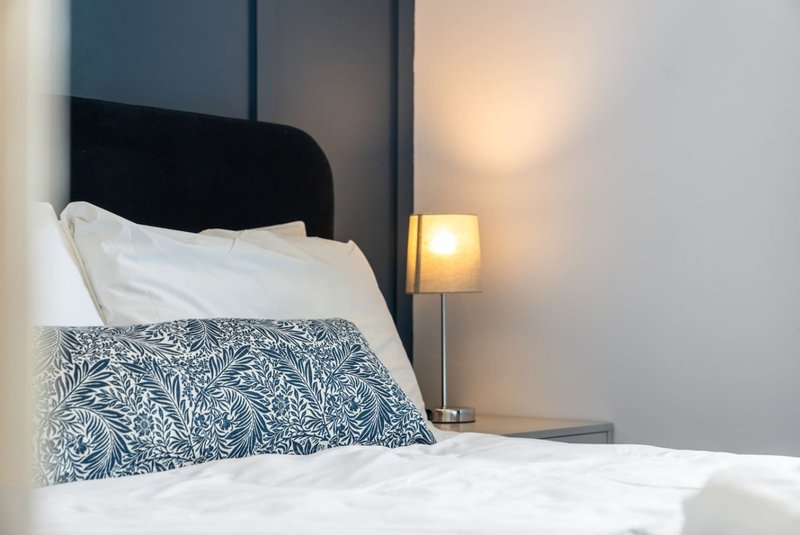 Modern bedroom with black headboard, white pillows, patterned cushion, and bedside lamp