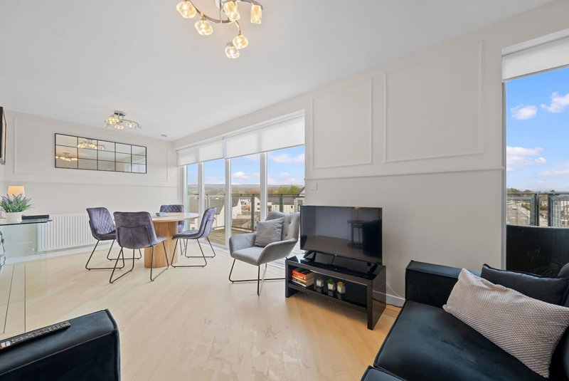 Spacious open-plan living area with dining table, black sofa, TV, and large windows overlooking landscape
