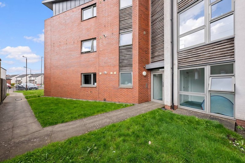 Modern brick apartment building exterior with green lawn and paved pathway