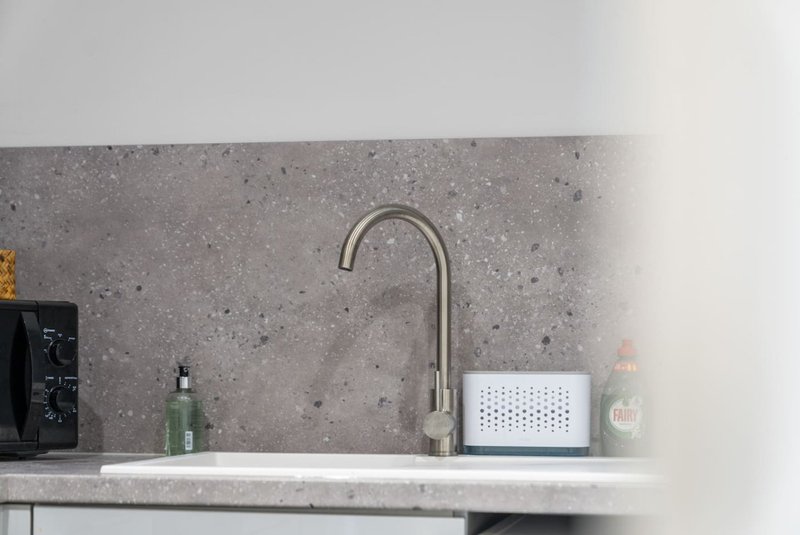 Modern kitchen sink with stainless steel tap and concrete backsplash