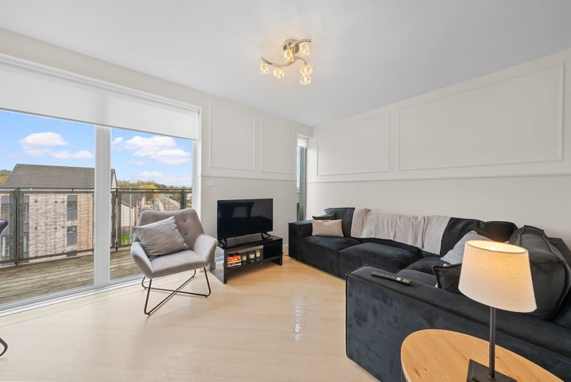 Bright living room with black sofa, armchair, TV, wooden floor and large patio doors overlooking garden