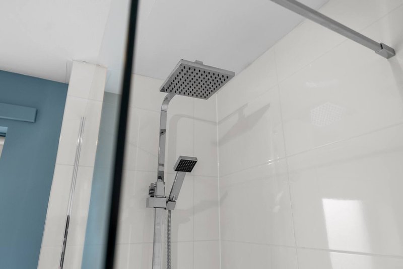 Modern bathroom shower enclosure with rainfall showerhead, white tiles and blue accent wall
