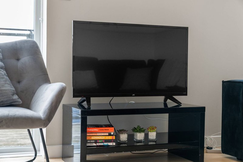 Living room with television on black stand, gray armchair, and window with natural light