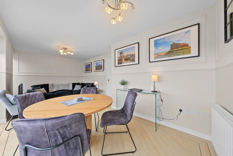 Modern dining area with round wooden table, purple chairs, sofa, framed wall art and pendant lighting