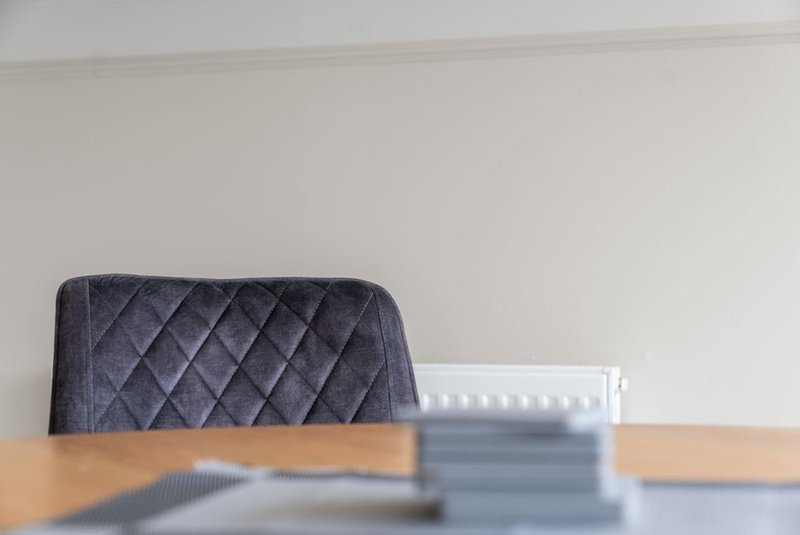 Wooden dining table with quilted grey chair and minimalist white wall background
