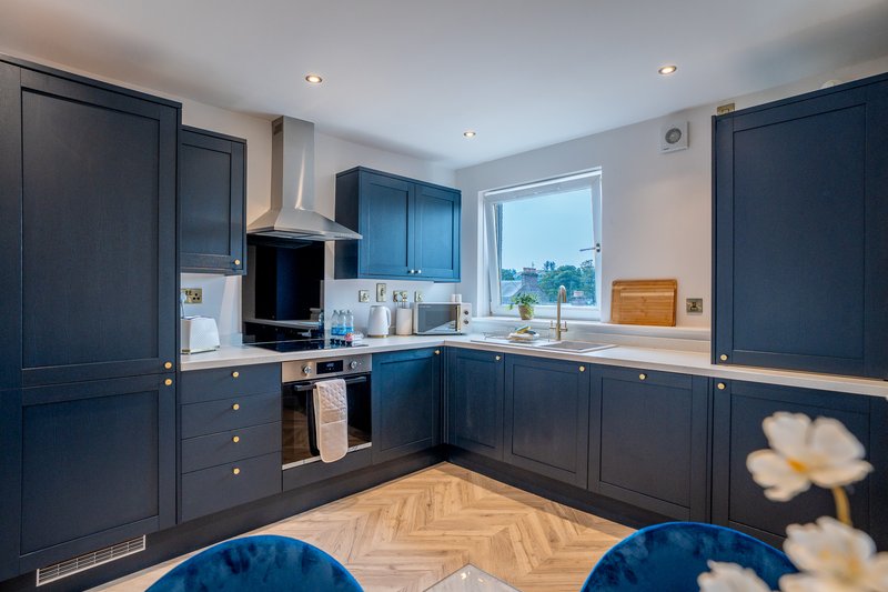 Modern kitchen with dark blue cabinetry, stainless steel appliances, and herringbone wood flooring