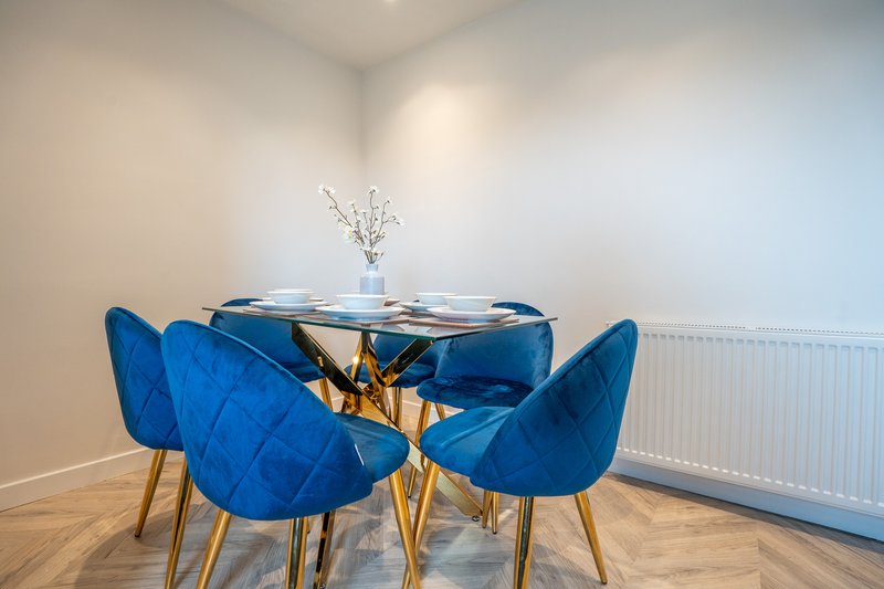 Modern dining area with round glass table, four blue velvet chairs, and white flowers in vase