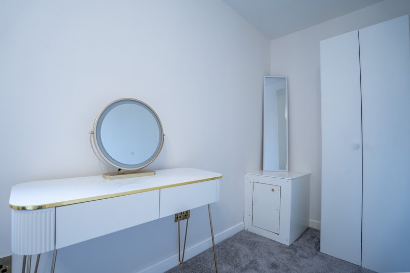 Modern bedroom with white vanity, round mirror, and full-length mirror on wall