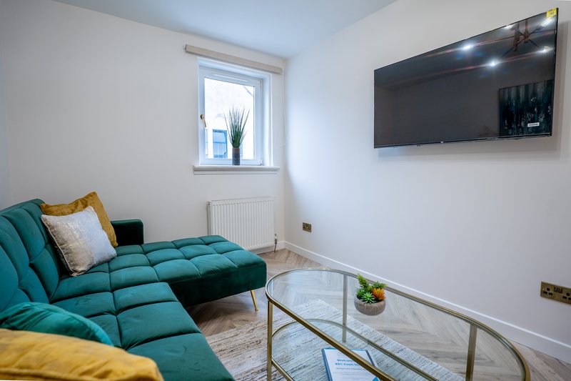 Modern living room with teal sectional sofa, wall-mounted TV, glass coffee table and window