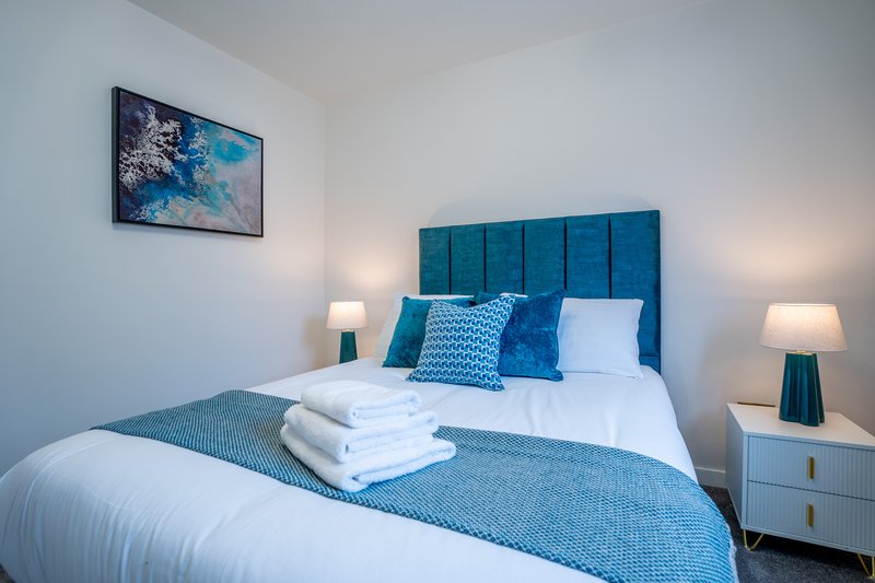 Modern bedroom with blue upholstered headboard, white bedding, blue throw blanket, and bedside lamps
