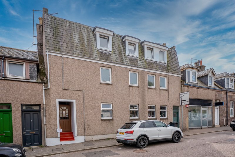 Exterior of brick townhouse with red door, parked car, and neighboring shops