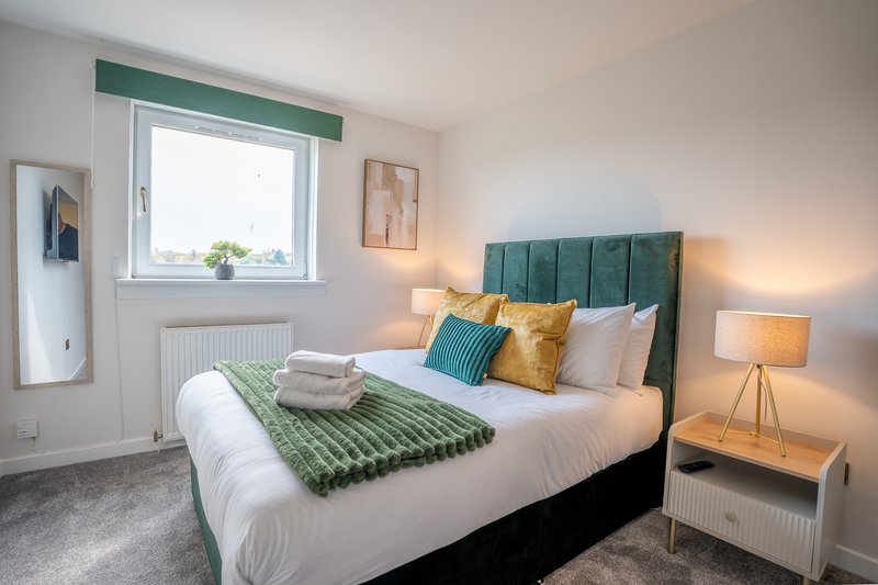 Bright bedroom with green upholstered headboard, white bedding, matching cushions and throws