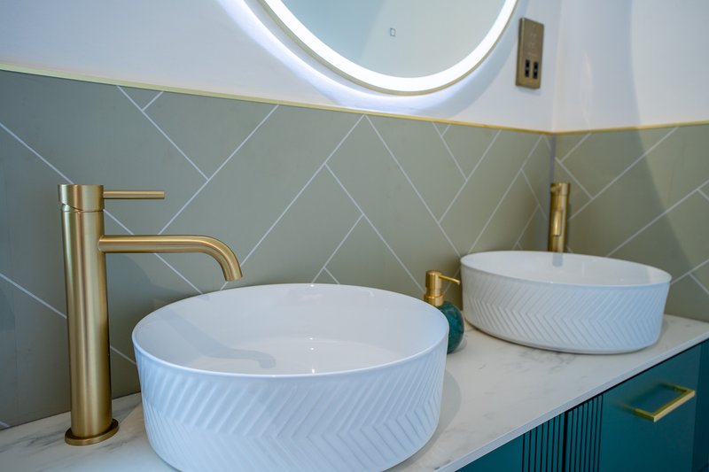 Modern bathroom with double vanity, round white vessel sinks, brass faucets and LED mirror