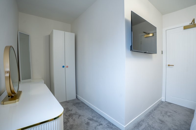 Modern bedroom corner with white wardrobe, dressing table, wall-mounted TV and grey carpet flooring