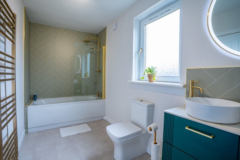 Modern bathroom with white toilet, teal vanity, vessel sink, shower tub and window