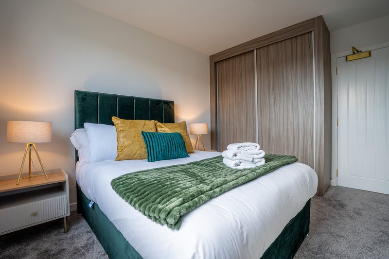 Modern bedroom with green upholstered bed, white bedding, yellow and teal cushions, and bedside lamps