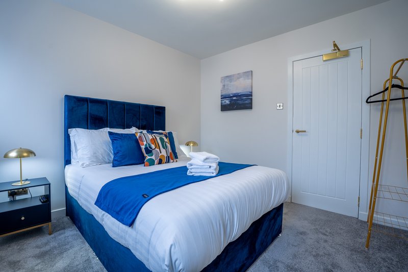Modern bedroom with blue upholstered bed, white bedding, gold accents, and white door