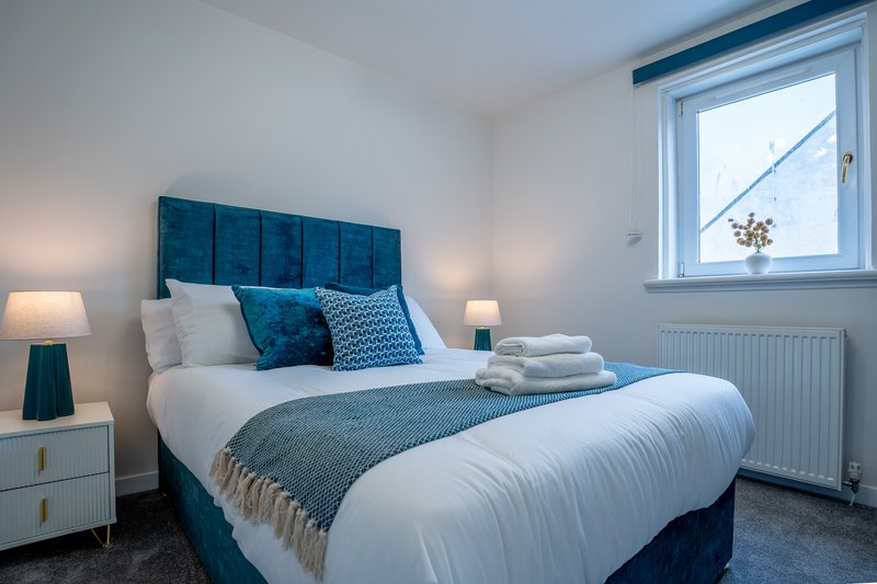 Modern bedroom with teal upholstered bed, white bedding, decorative pillows and folded towels