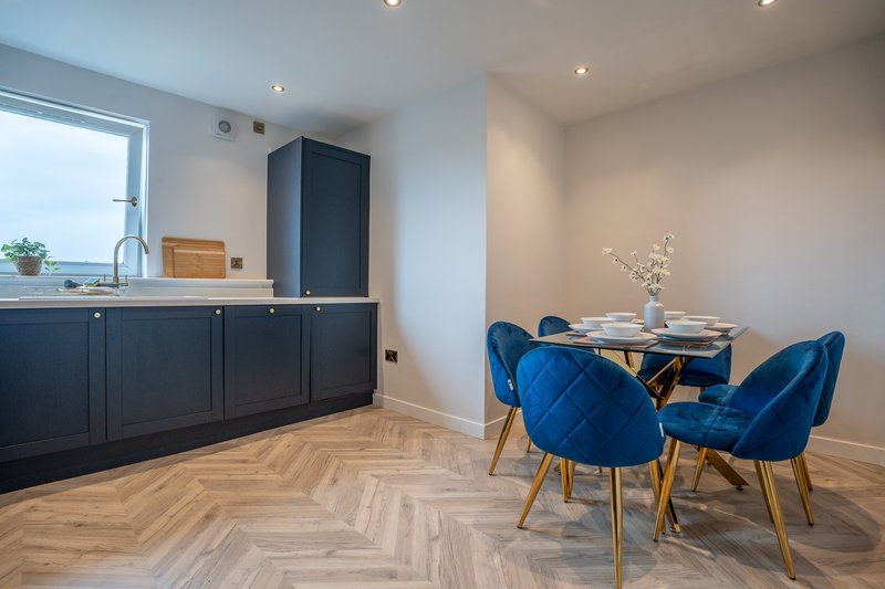 Open-plan kitchen and dining area with dark cabinetry, wooden herringbone flooring, blue velvet chairs