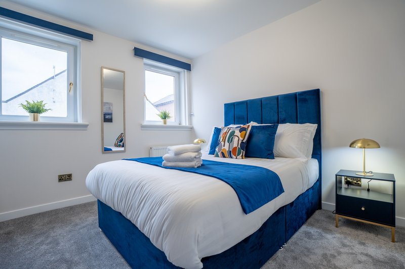 Modern bedroom with blue upholstered bed, white bedding, gold lamp and windows