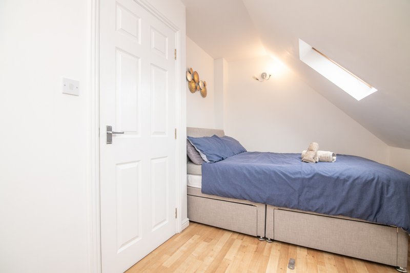Bright attic bedroom with blue bedding, wooden floor, white door and skylight