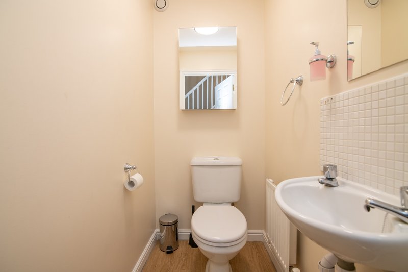 Small bathroom with toilet, pedestal sink, mirror, and tiled wall