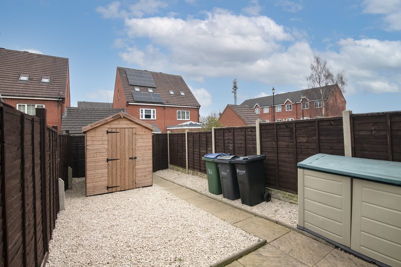 Rear garden with sheds, fencing, gravel surface and neighbouring brick houses
