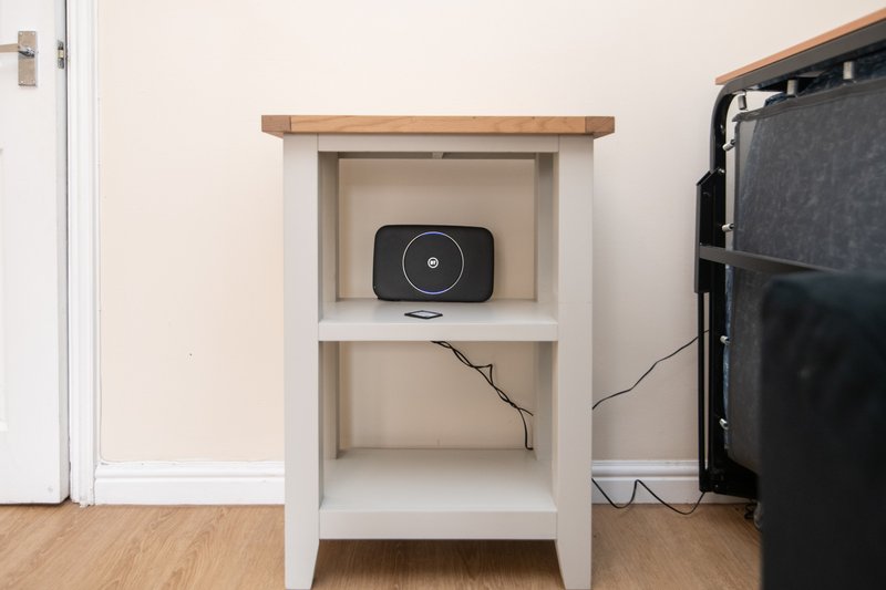 White wooden shelving unit with device on upper shelf, wooden floor, TV on right