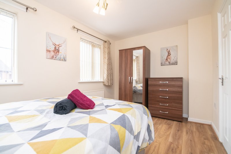 Bright bedroom with double bed, geometric patterned duvet, wooden wardrobe and chest of drawers