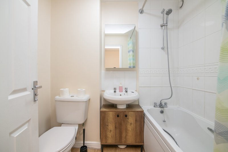 Clean bathroom with toilet, wooden vanity, sink, mirror and bathtub with shower