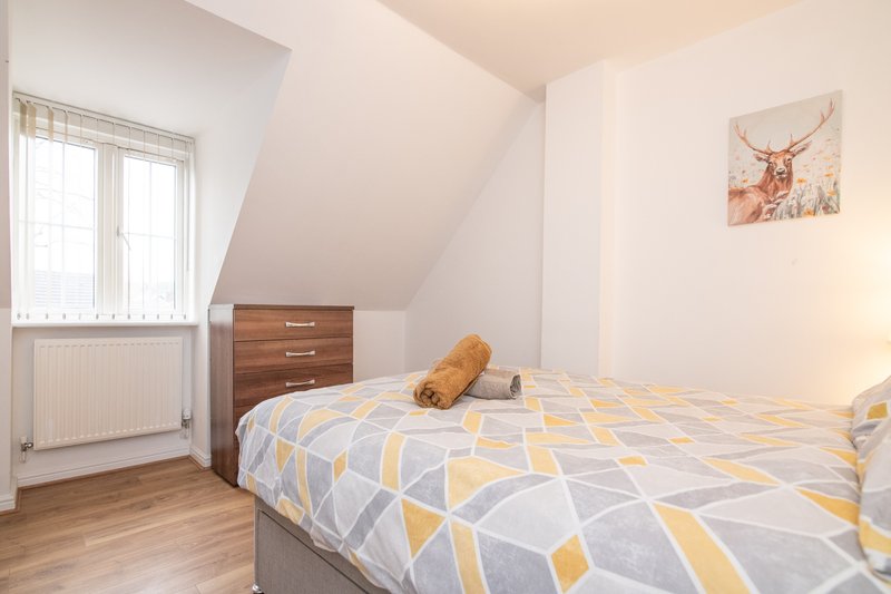 Bright attic bedroom with double bed, wooden dresser, window and wall art