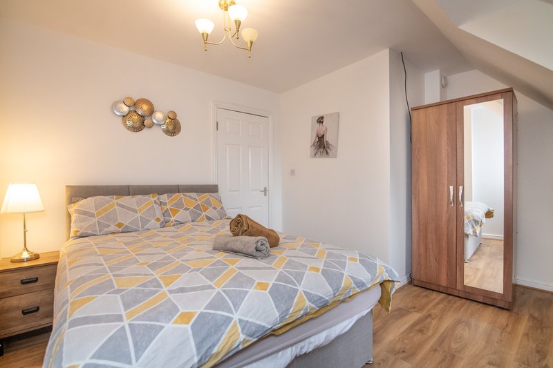 Bright bedroom with double bed, geometric bedding, wooden wardrobe and bedside lamp