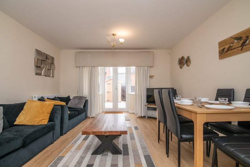 Open-plan living and dining room with sofa, wooden table, desk area and glass doors to patio