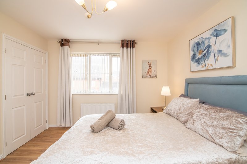 Bright bedroom with double bed, blue headboard, wooden floor and large window