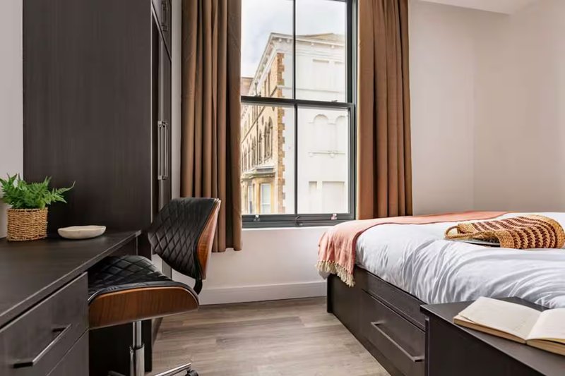 Modern bedroom with double bed, desk chair, window with city view and brown curtains