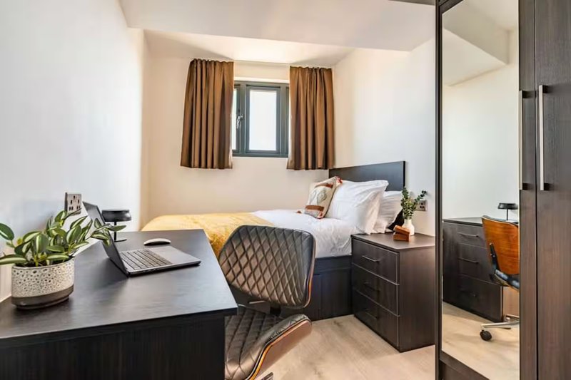 Compact bedroom with desk, chair, double bed, dark wood furniture and mirror