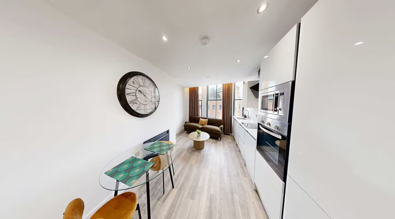 Modern open-plan kitchen and dining area with white cabinetry, wooden flooring, and wall clock