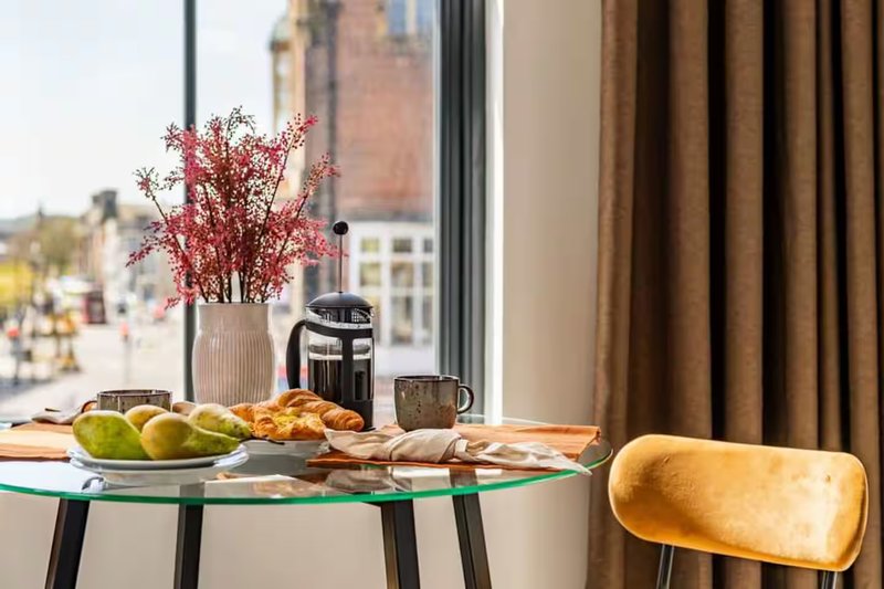Modern dining table by window with fresh fruit, pastries, flowers and city view