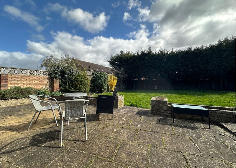 Spacious garden patio with seating area, stone walls, hedges and lawn