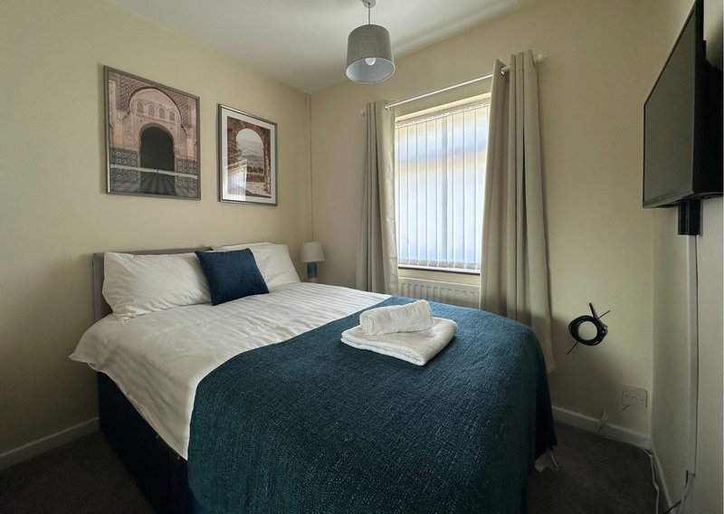 Bedroom with double bed, blue throw, white pillows, framed wall art and window with blinds