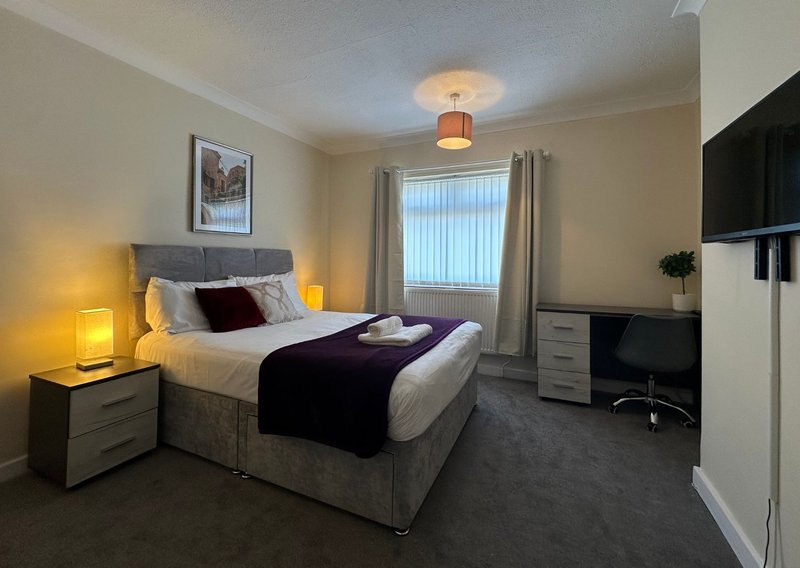 Bright bedroom with double bed, two bedside lamps, desk area and wall-mounted TV